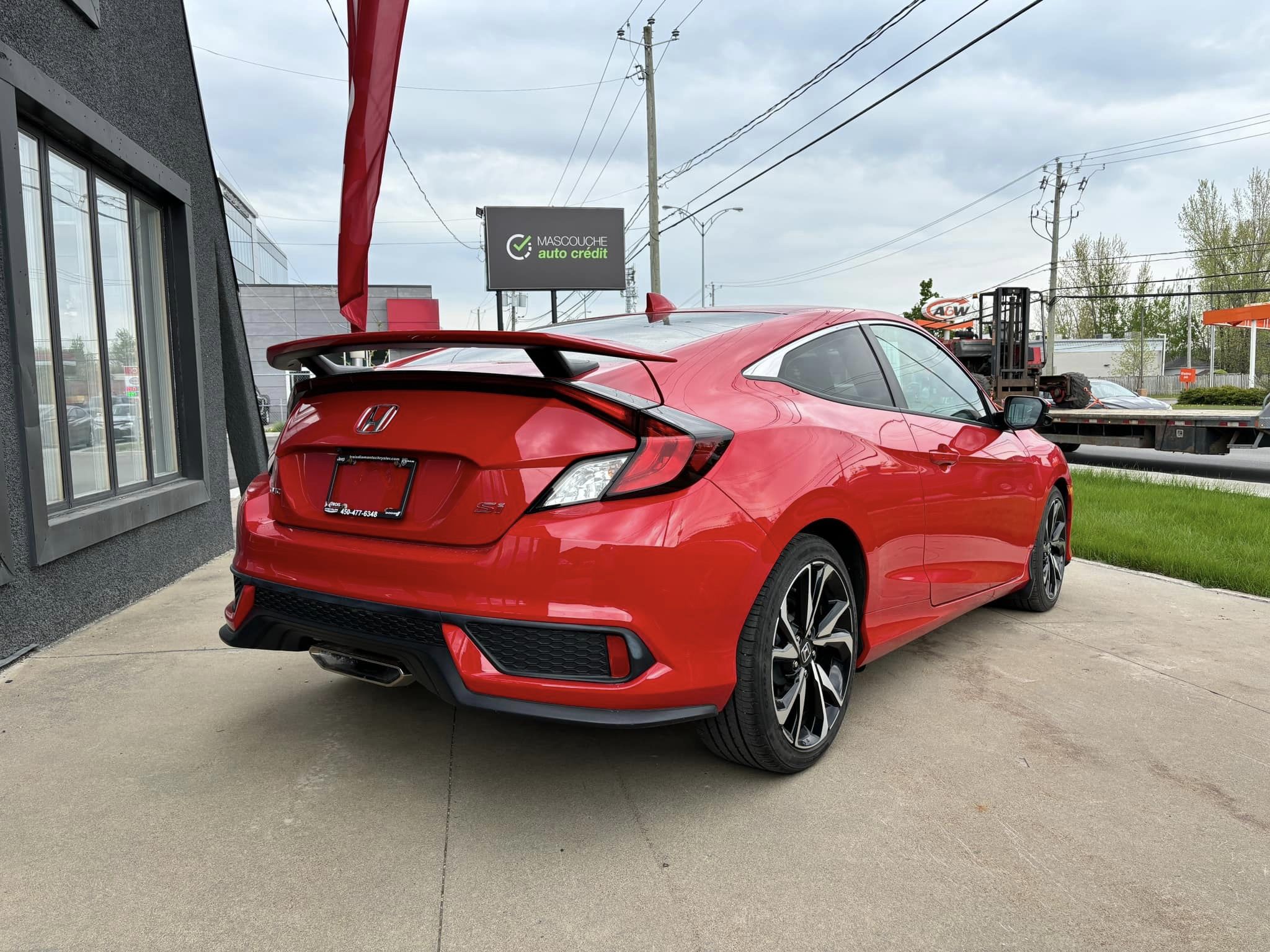 Vue arrière d'une Honda Civic rouge garée devant un concessionnaire. Le véhicule présente des lignes sportives, des jantes en alliage noir et un aileron arrière. Un panneau de crédit auto Mascouche est visible en arrière-planule, gestion des dettes.